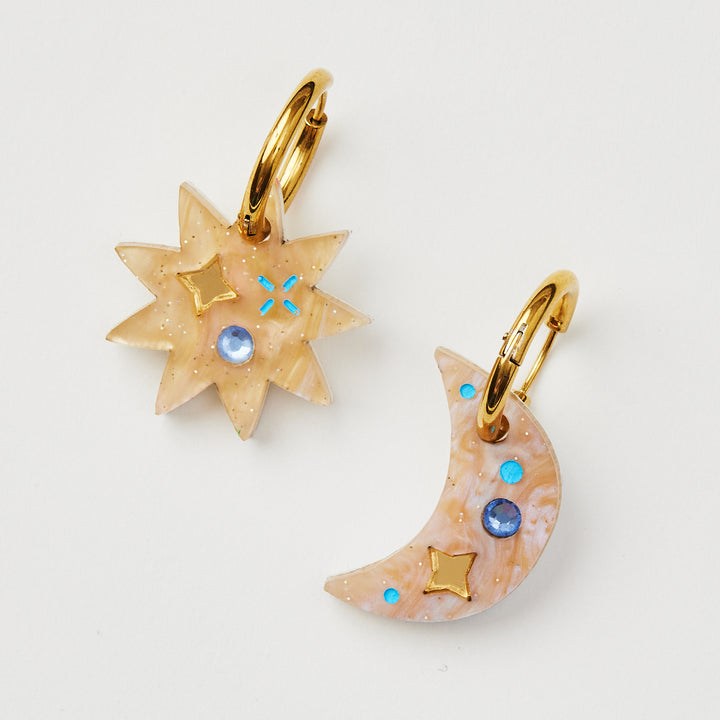mismatched star and crescent earrings with twinkling motifs and a dazzling crystal inlay hanging on a gold hoop 