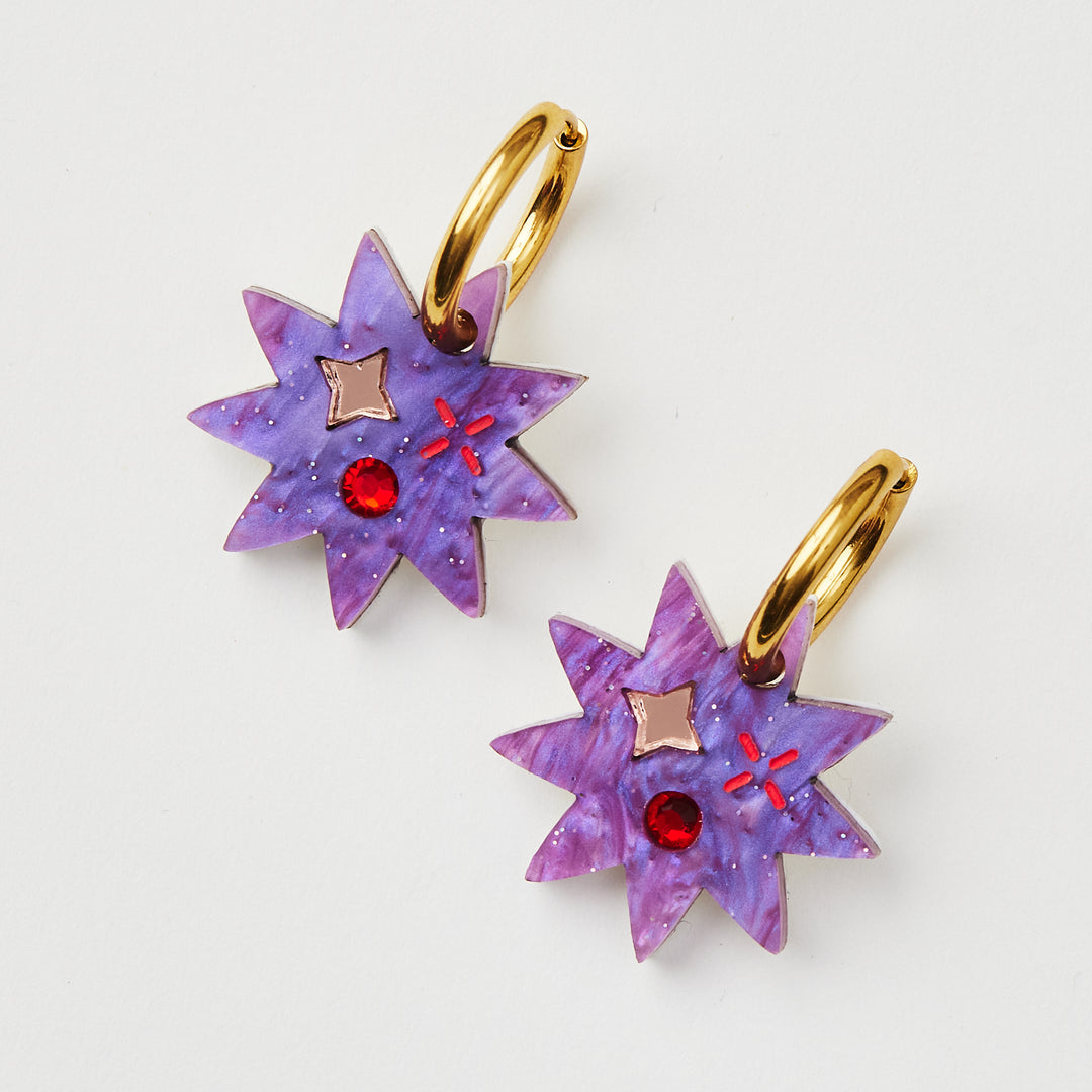 Purple Star earring with twinkling motifs and red crystal inlay hanging on a gold hoop 
