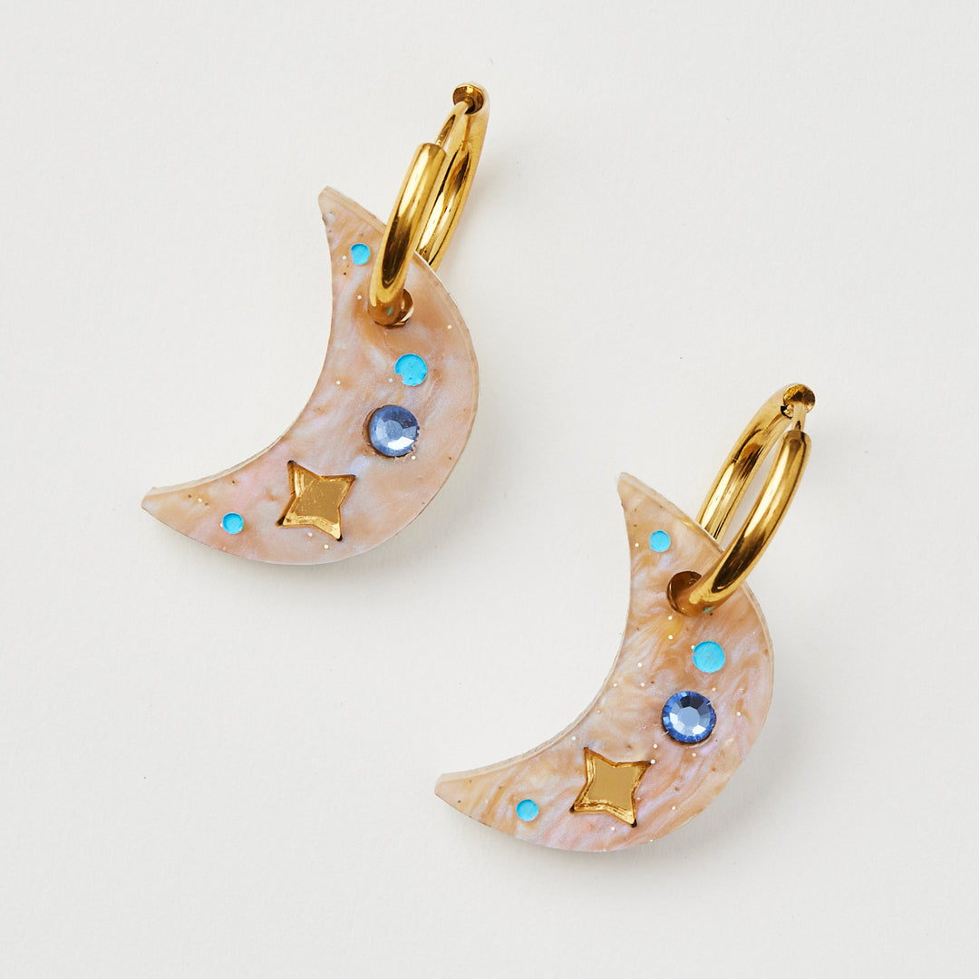 Moon earring with twinkling motifs and blue crystal inlay hanging on a gold hoop 
