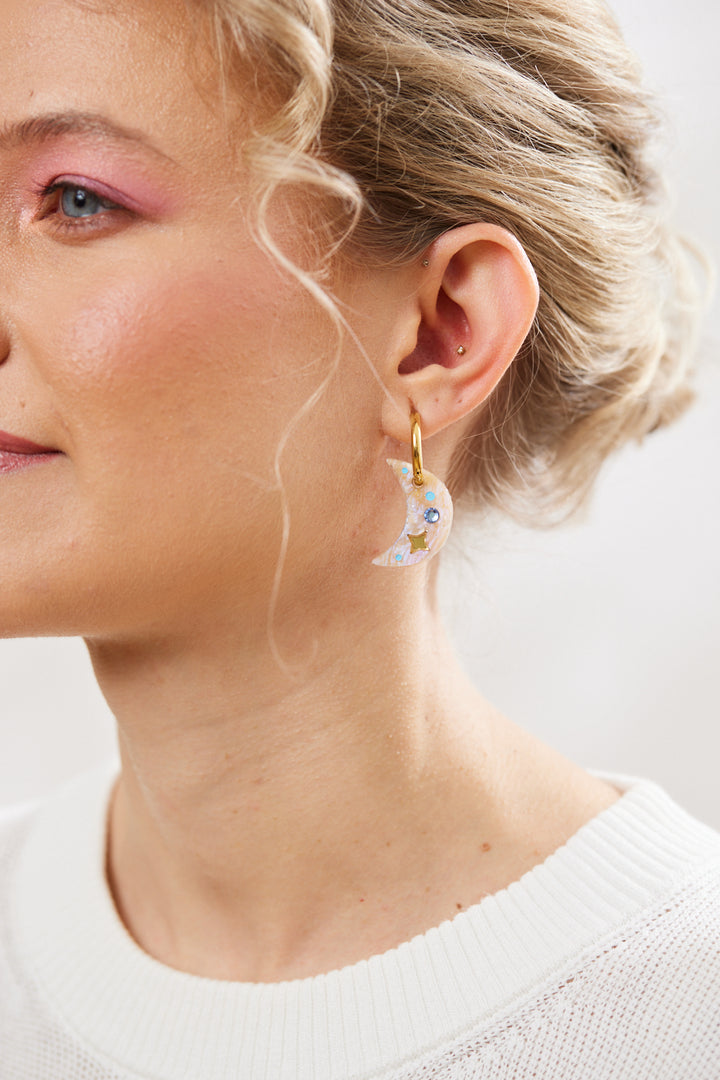 crescent earring with twinkling motifs and crystal inlay hanging on a gold hoop  pictured on a model