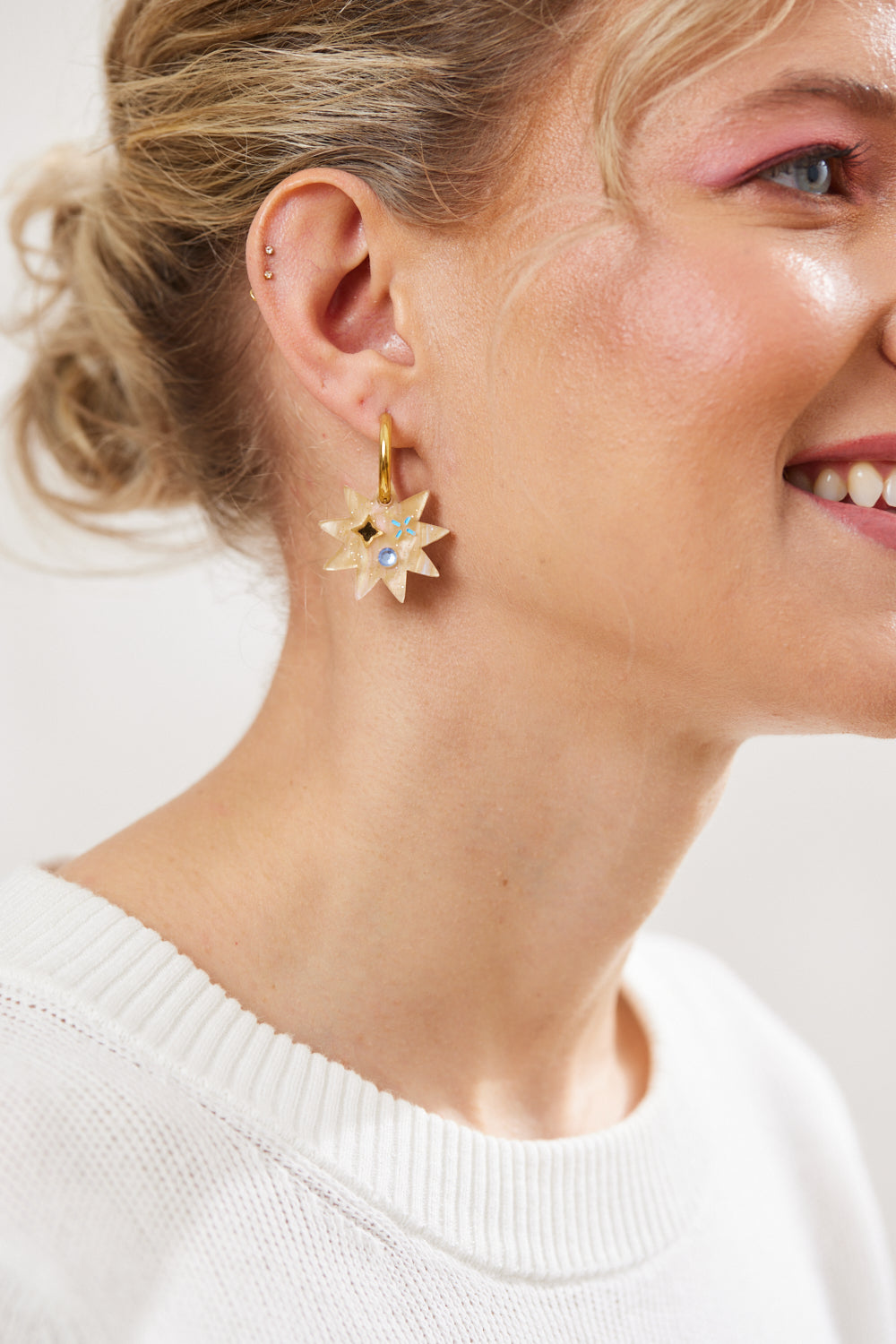 Star earring with twinkling motifs and crystal inlay hanging on a gold hoop  pictured on a model