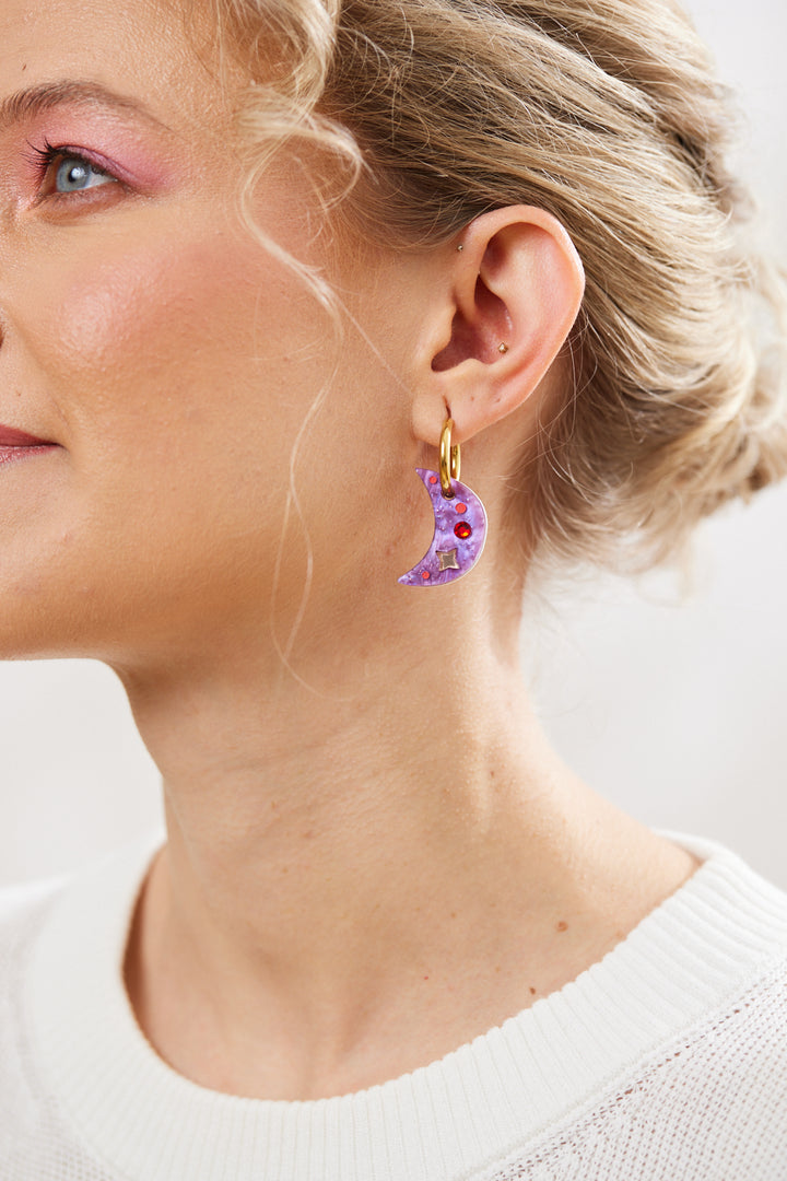 Purple crescent earrings with twinkling motifs and a dazzling red crystal inlay hanging on a gold hoop 