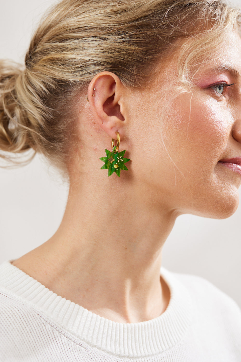 Green Star earring with twinkling motifs and yellow crystal inlay hanging on a gold hoop  pictured on a model