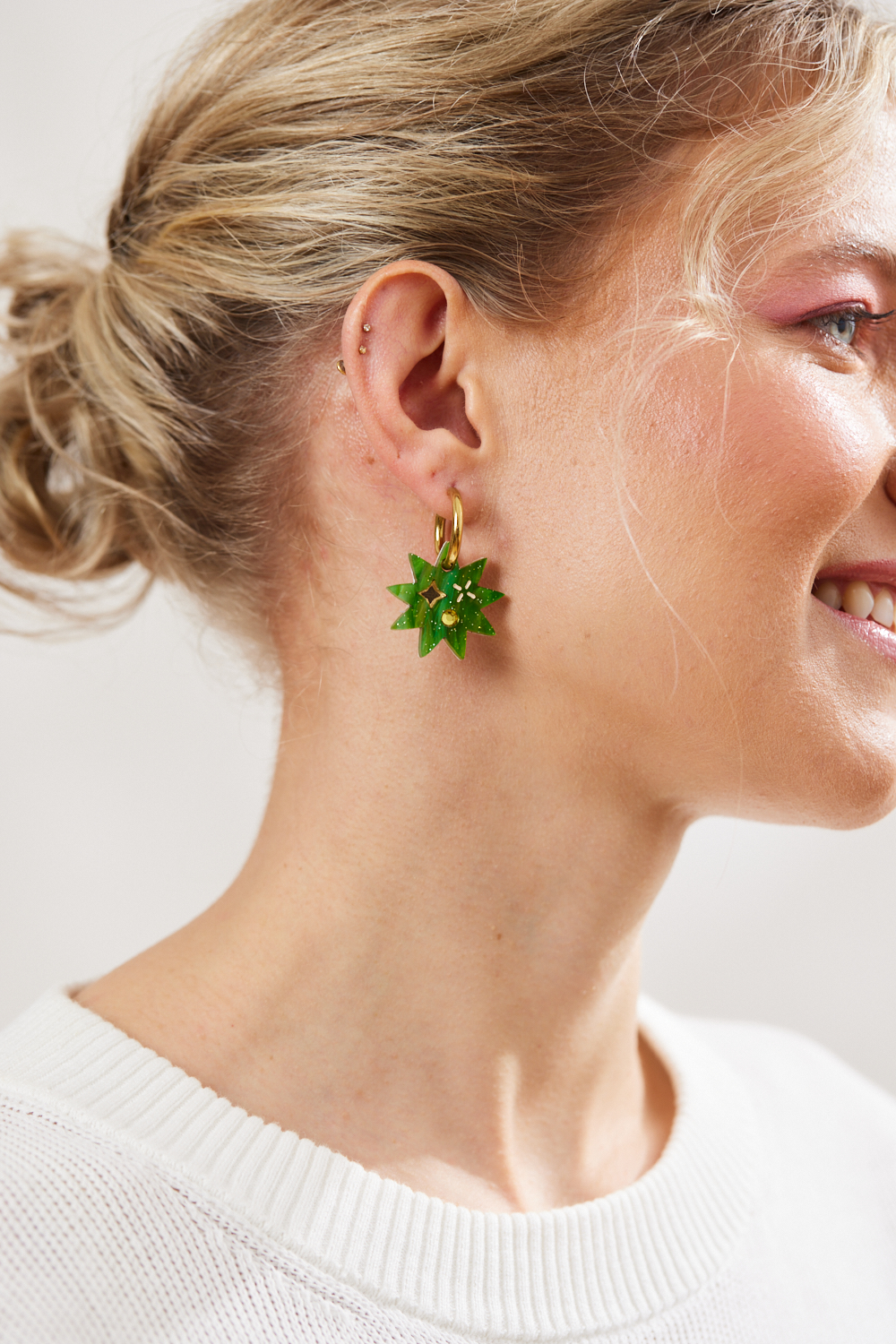 Green Star earrings with twinkling motifs and a dazzling crystal inlay hanging on a gold hoop pictured on a model 