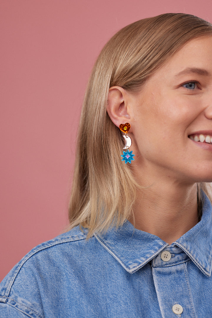 Model wearing earrings with a heart, moon and star. 